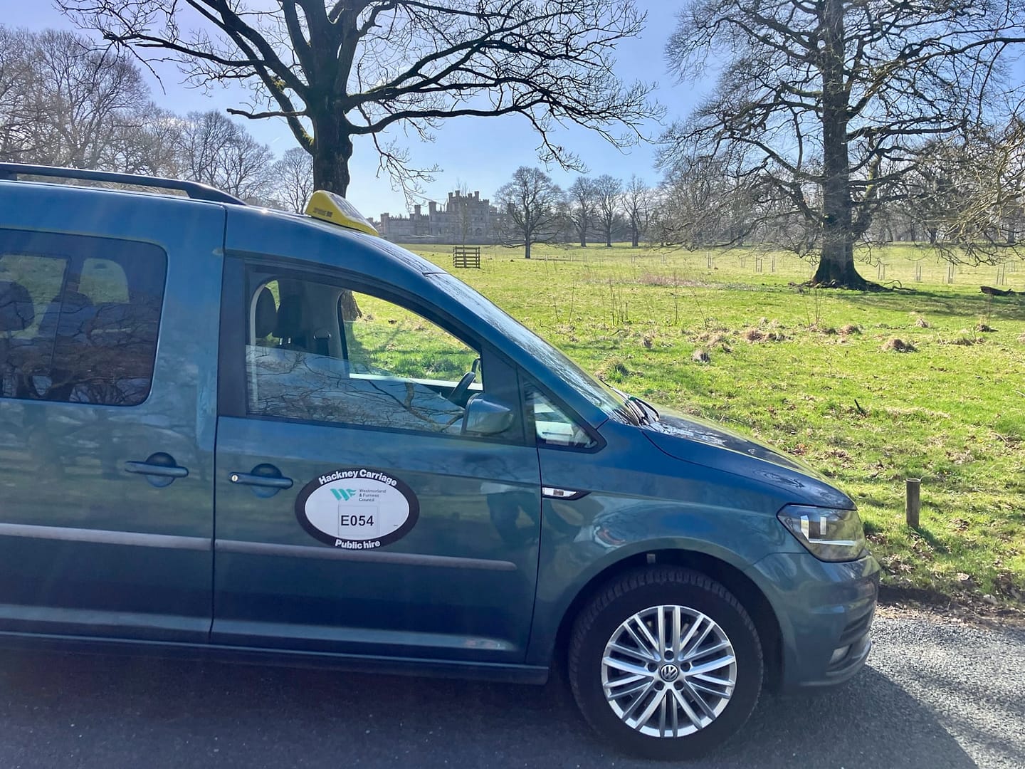 Fell Cabs parked on a sunny day with Lowther Castle in the background
