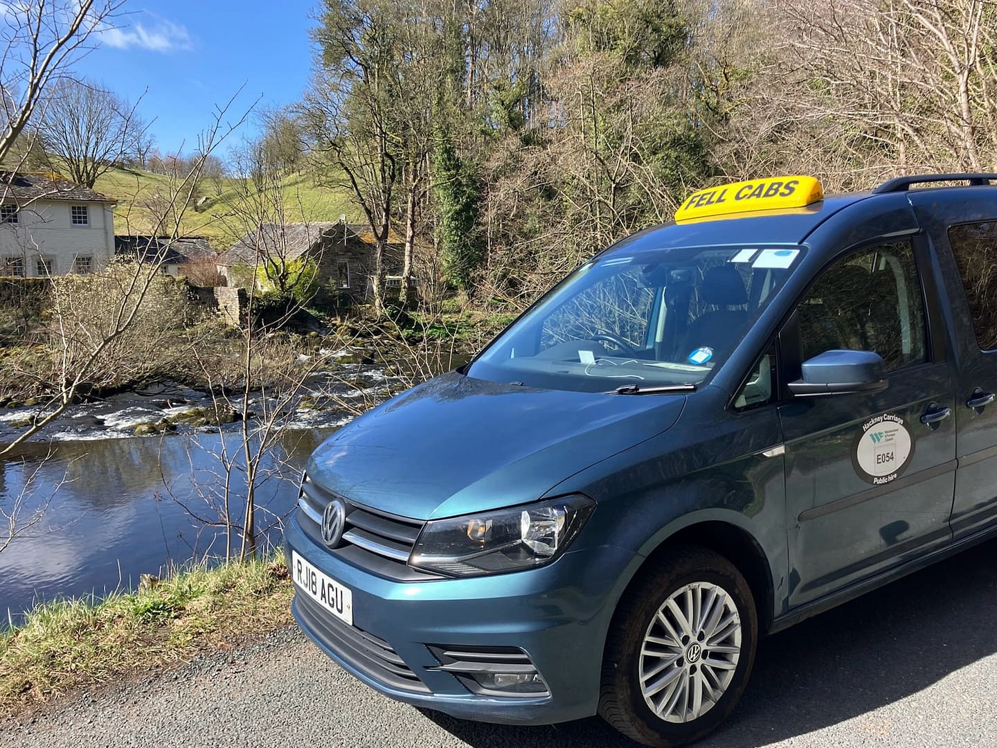 Fell Cabs parked by a picturesque river and countryside in the Lake District